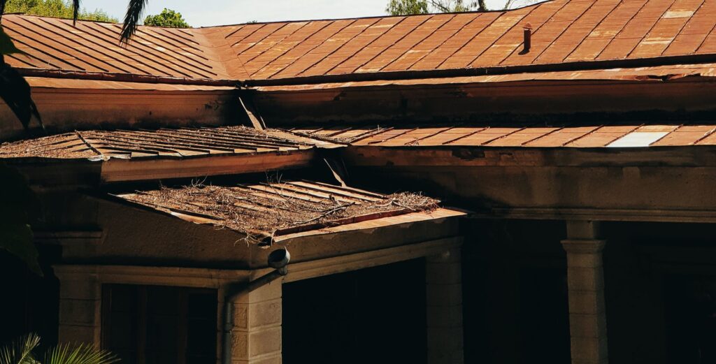 A rustic building with a red-tiled roof surrounded by lush palm trees under a clear sky.